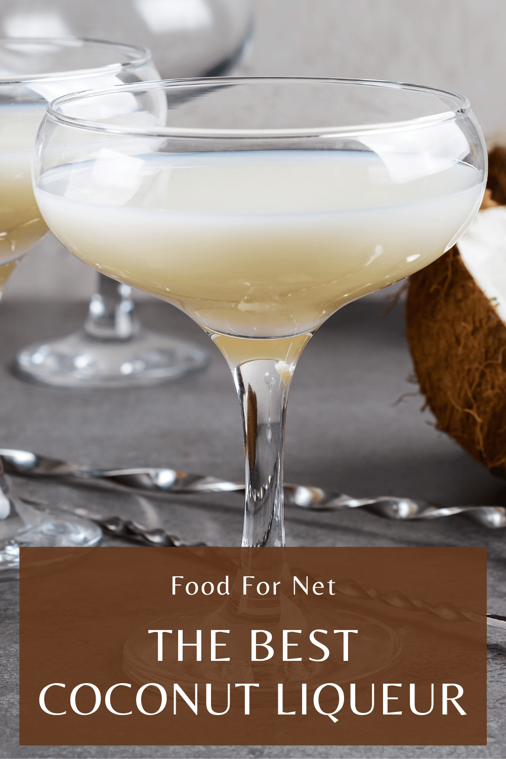 Two glasses of coconut liqueur on a table, next to some coconuts and a stirring spoon