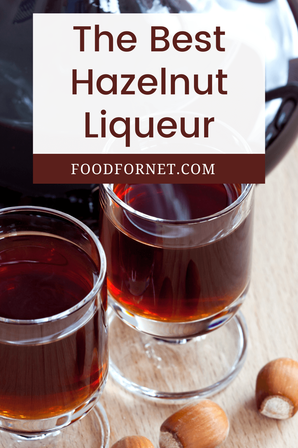 Two glasses and a large jug of hazelnut liqueur, with a few hazelnuts on the table