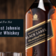 A bottle of Johnnie Walker Black next to a glass of the whiskey on a table in front of a wooden wall