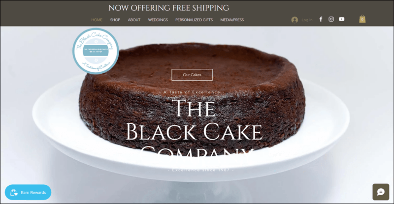 screenshot of The Black Cake Company's web page, with a dark moss green banner on top bearing the main navigation menu, followed by a white content area showing an image of a whole Black Cake with text overlay and the website's logo at the upper left side