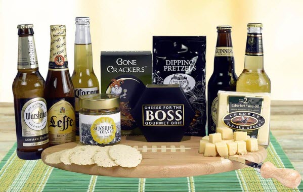 A selection of beers and snacks surrounding a football cutting board. There are also some snacks on the board itself. 