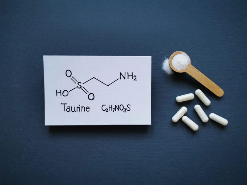 The chemical formula of taurine on a piece of paper, next to capsules, and some powder