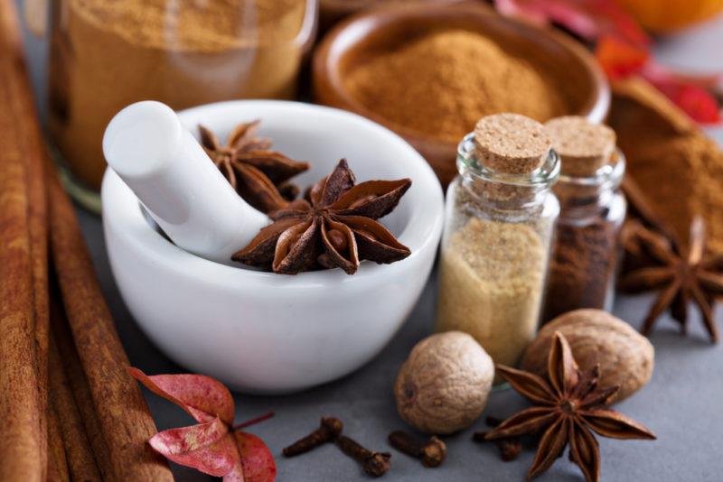 A white mortar and pestle, with various spices to make pumpkin pie spice