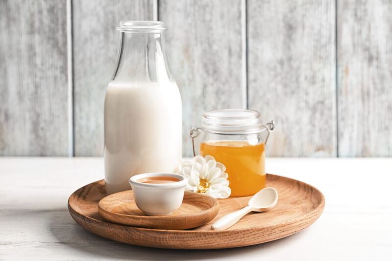 A bottle of milk, a jar of honey, and a small dish that may contain cognac, all the ingredients to make a snow honey cocktail