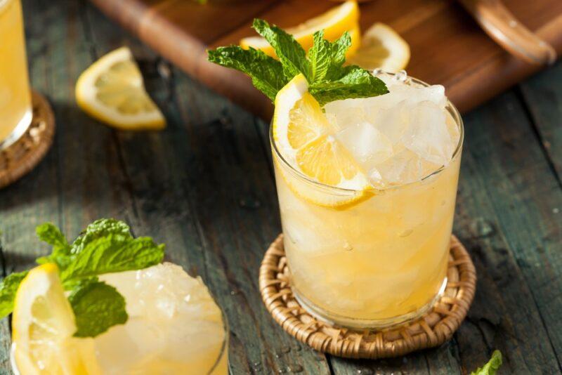 Two lemon beat cocktails on coasters on a table, with plenty of ice and a lemon wedge