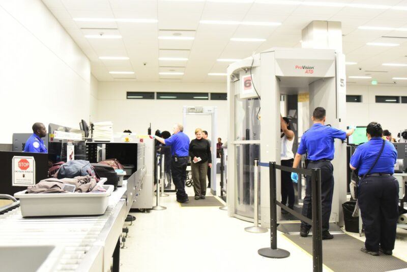 The security screening line at an airport, where the security guards are wearing blue shirt