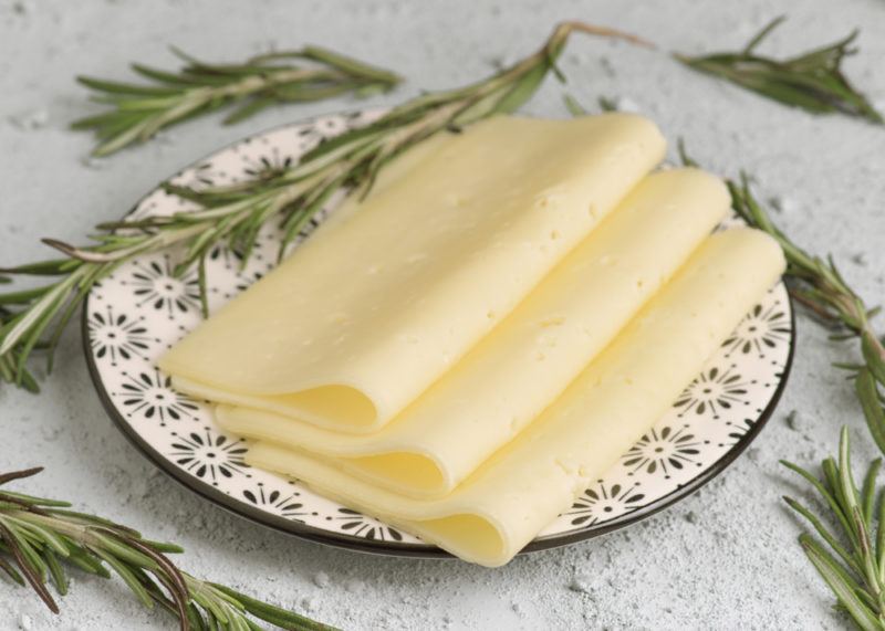 Thin slices of harvarti cheese on a white plate with rosemary