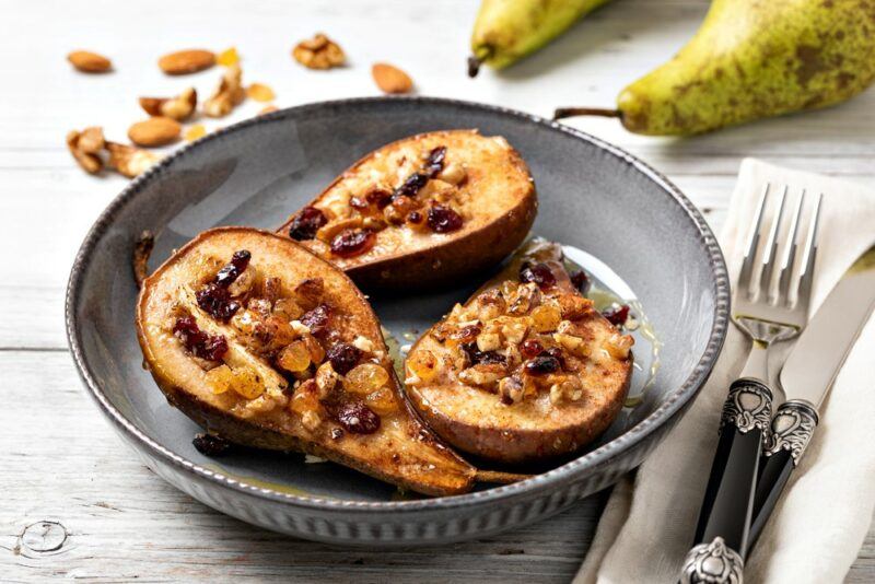 A gray bowl with three baked pears and raisins