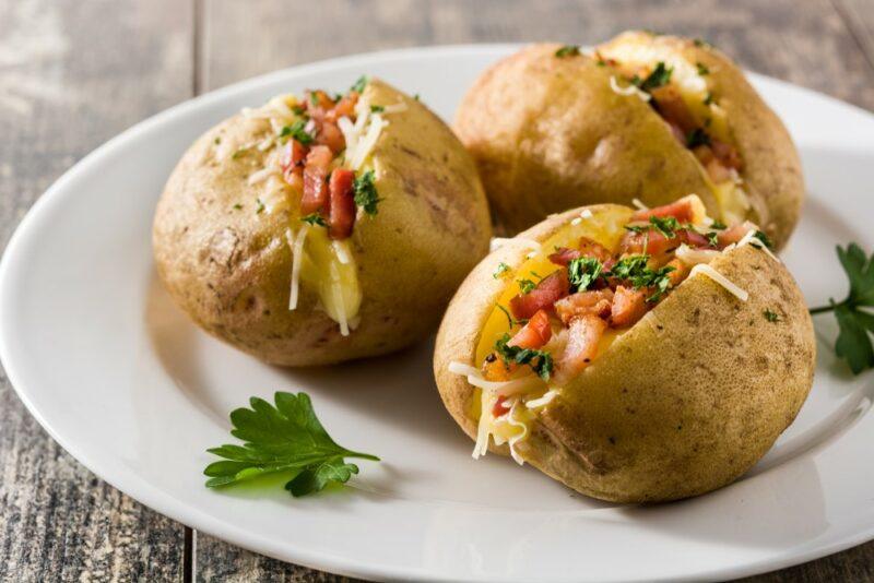 Three baked potatoes on a plate with cheese and bacon