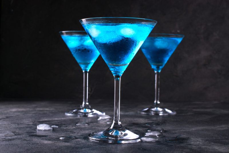 Three electric blue martinis on a gray table against a black background