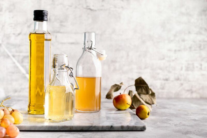 A table with apples and grapes, along with three bottles containing different types of vinegar