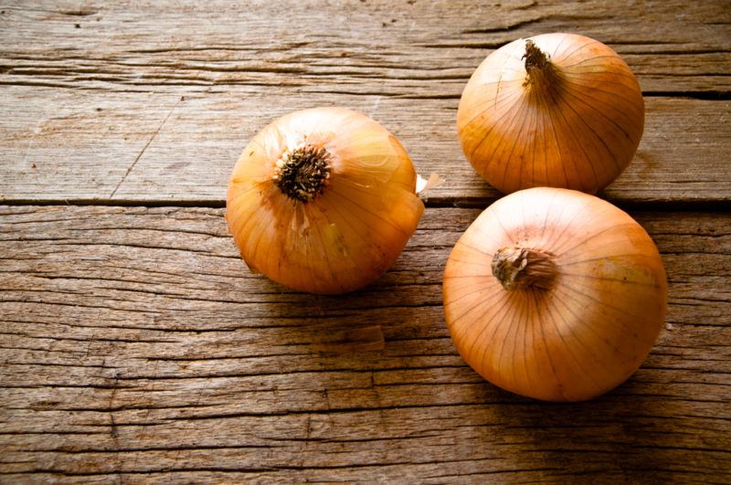 Three brown onions on a wooden table