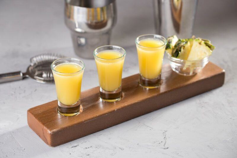 Three yellow char'd pineapple shots on a wooden board