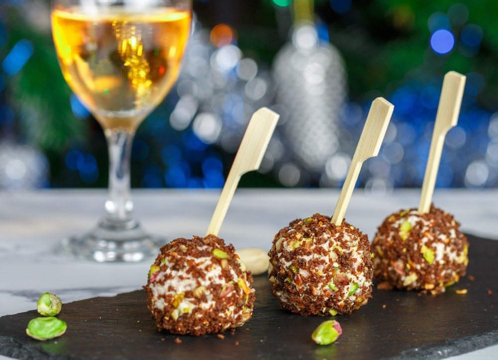 Three cheese balls on a wooden plate with tooth picks, with a glass of wine in the background