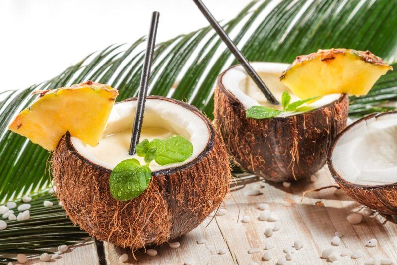 Two coconut halves filled with a batida de coco cocktail, in front of a leaf from a coconut tree