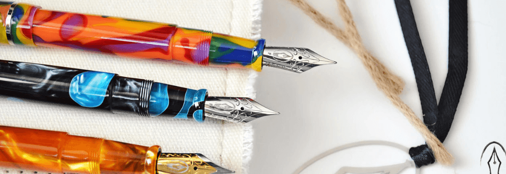 Three colorful ornate fountain pens laid out on a white cloth