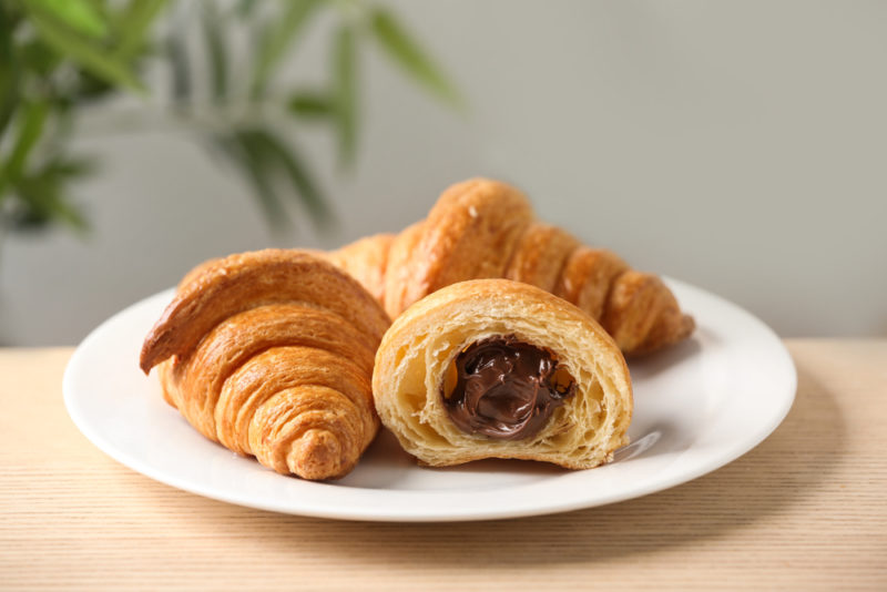 A white plate containing two croissants and a third one that is cut in half with a chocolate filling