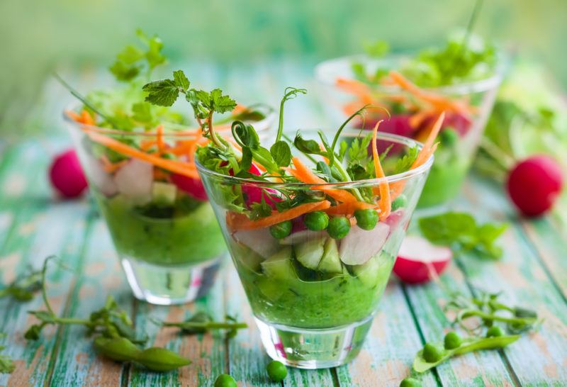 Three small glasses with vegetables and green hummus dip