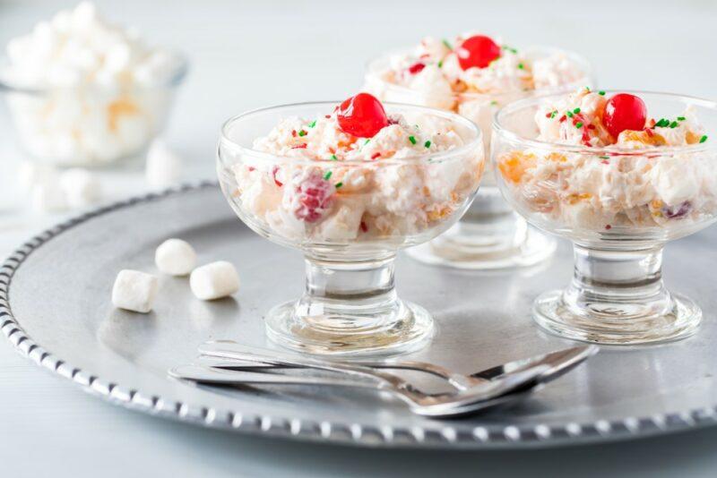 Three dessert glasses with a cheesecake fruit salad and a glace cherry as a garnish