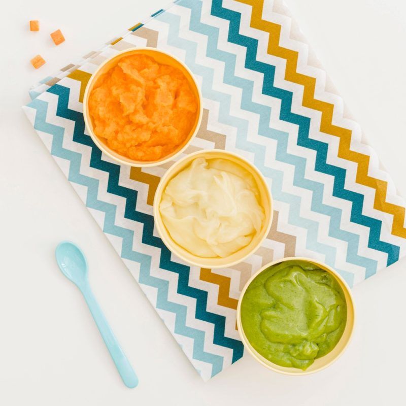 Three dishes of baby food, including carrots, cauliflower, and broccoli