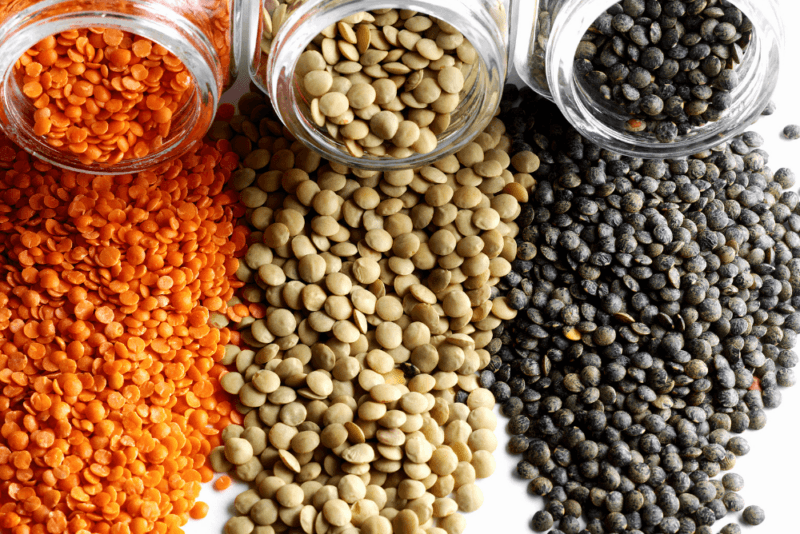 Three glass jars containing lentils of different colors spilling onto the table