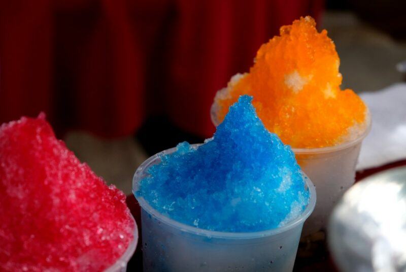 Three different flavors of snow cone, including boozy blue, orange, and red