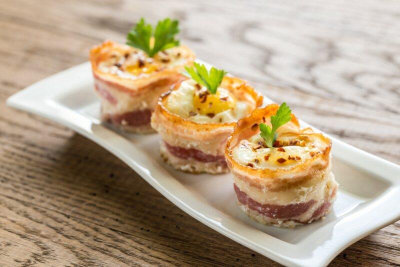 A white plate with three bacon and egg cups