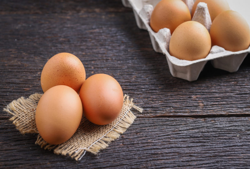 Three fresh eggs on a piece of cloth with a egg carton of eggs in the background