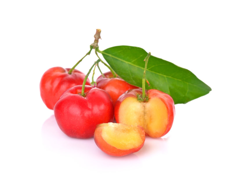 Three fresh Barbados cherries still on their stalks with a leaf and one that has been sliced