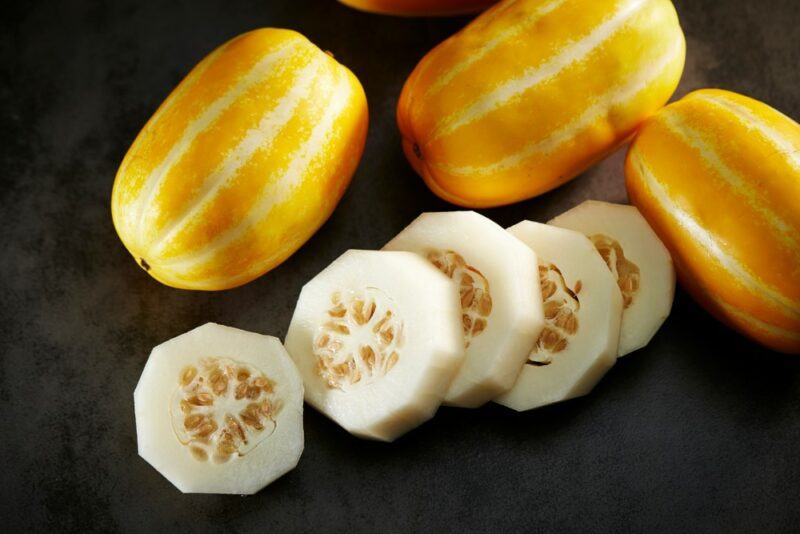 Three bright yellow striped Korean melons, along with some melon slices