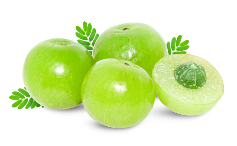 Four green alma berries with tiny leaves isolated on white, next to one that has been cut in half