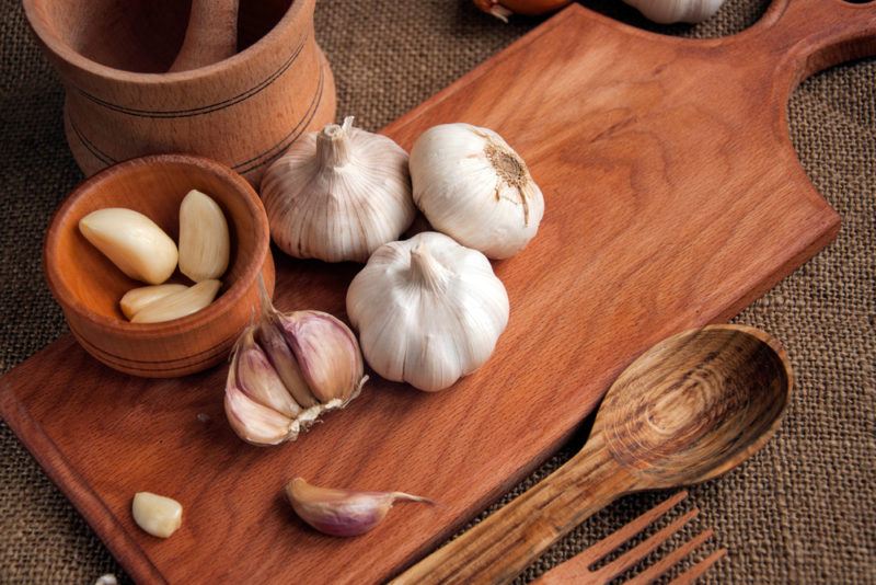 A wooden board with some bulbs of garlic and cloves of garlic in a bowl