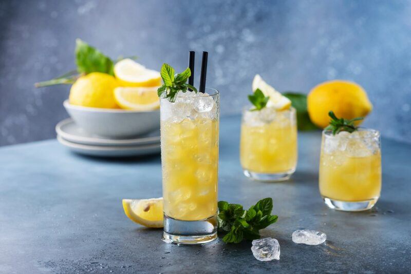 Three glasses of a Lynchburg lemonade cocktail with ice, in front of a bowl of lemons