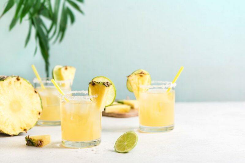 Three glasses containing a pineapple cocktail called In The August Sun