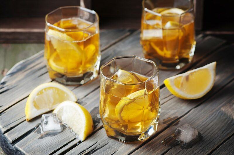 A wooden table with three glasses of a Mackinnon cocktail with ice and lemon wedges on the table