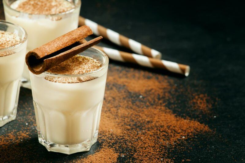 Three glasses of a bourbon milk punch on a black table with straws and cinnamon scattered around