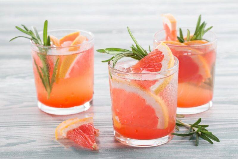 Three glasses of a grapefruit juice cocktail, with sliced grapefruit and sprigs of rosemary