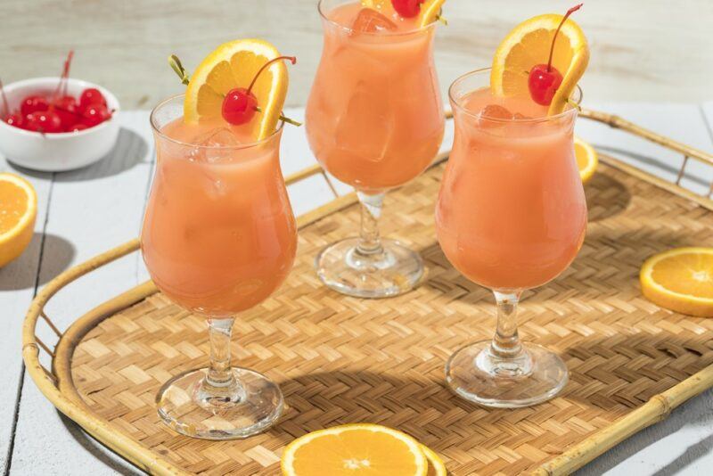 Three glasses of a hurricane cocktail garnished with a cherry and citrus slice