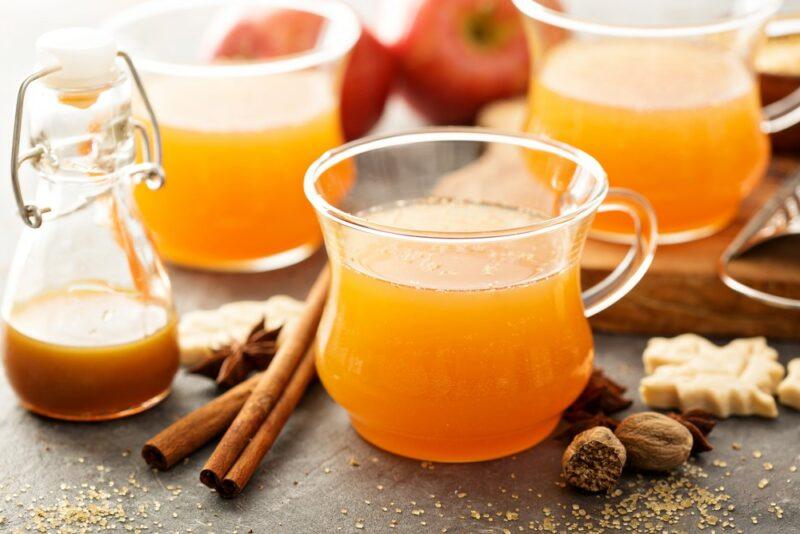 Three glasses of a rum caramel hot apple cocktail on a table with spices and a small jug of caramel