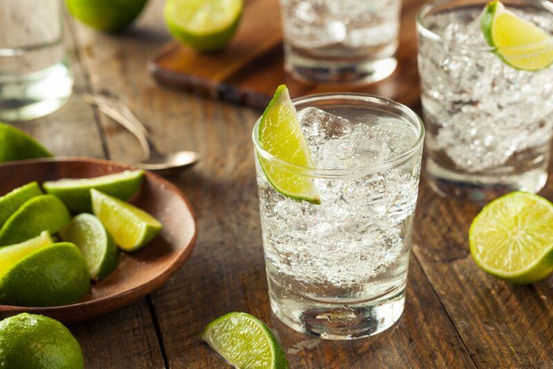 Three vodka tonic cocktails on a wooden table, next to lime wedges