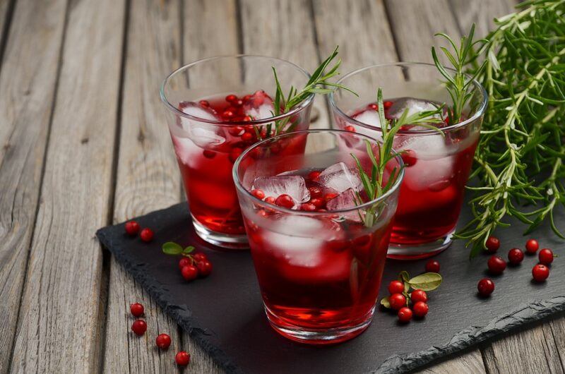 A black slate with a few glasses of cranberry juice with ice, next to some rosemary