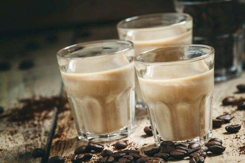 Three glasses of a homemade Baileys Irish Cream cocktail on a wooden table, surrounded by coffee beans