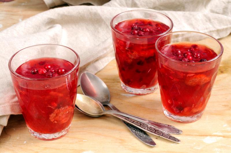 Three glasses of jello with fruit on a wooden board with spoons