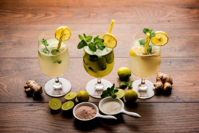 Three glasses of shikanji, an Indian drink, with various ingredients scattered in front of the glasses