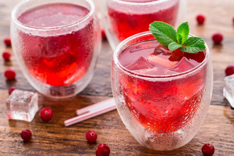 Three glasses of cranberry and soda water with cranberries scattered across the table