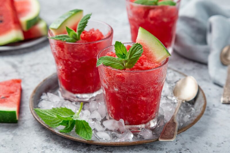 Three glasses containing fresh watermelon granita, with some watermelon elsewhere on the table