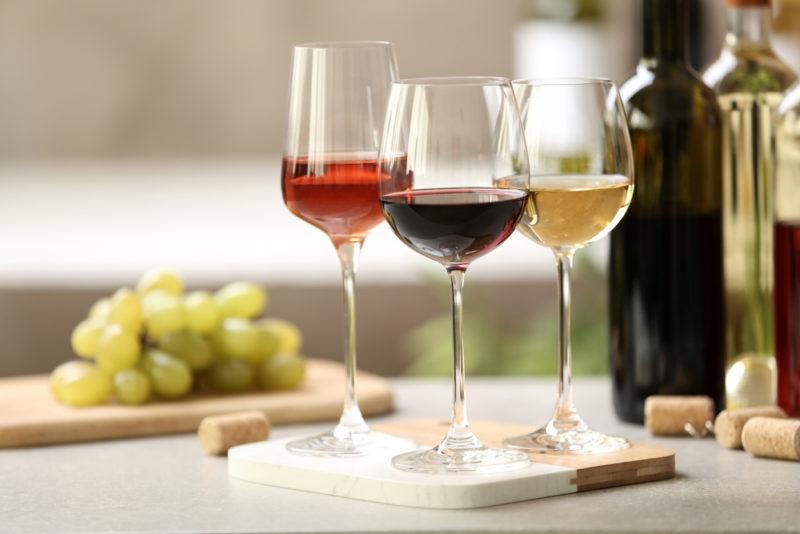 A glass of rose, a glass of red wine, and a glass of white wine, next to some bottles of wine