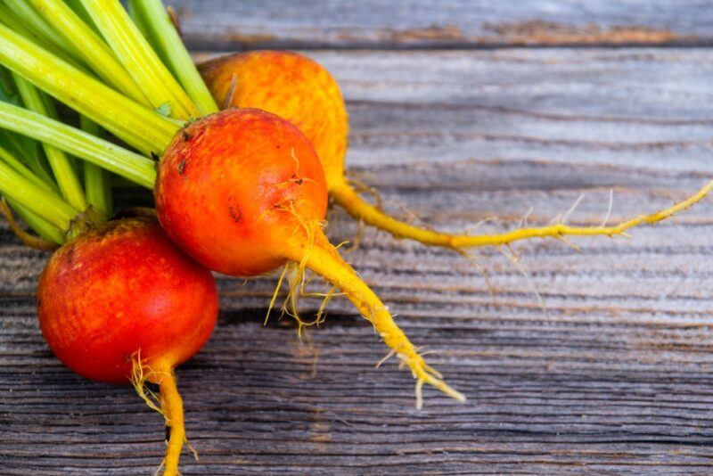 A wooden table with three golden beets with green stalks