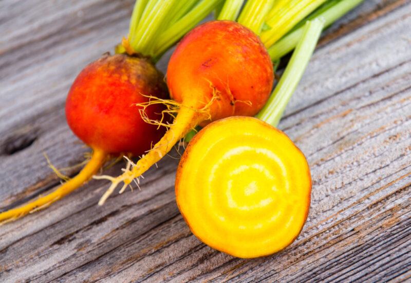 Three golden beets on a wooden table, one that has been cut in half