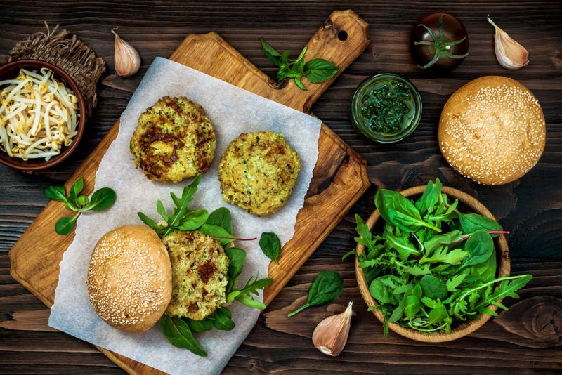 A wooden board on a table containing three homemade vegan patties, one of which is in a burger